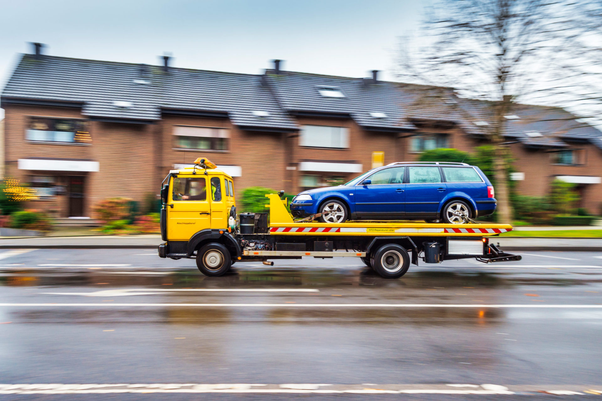 Pannenhilfe Abschleppdienst gelber Transporter mit Auto in blau und Warnmarkierung