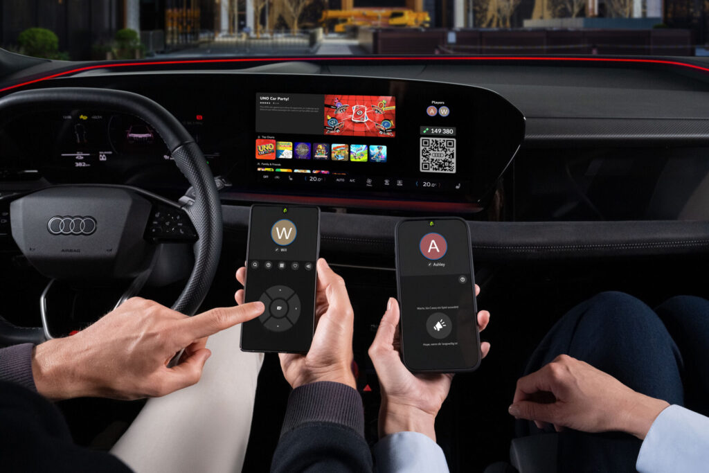 The AirConsole gaming platform app runs on the touch display in an Audi. The driver and front passenger each hold a smartphone in their hands in front of the display. They use the smartphones as controllers to play the games.